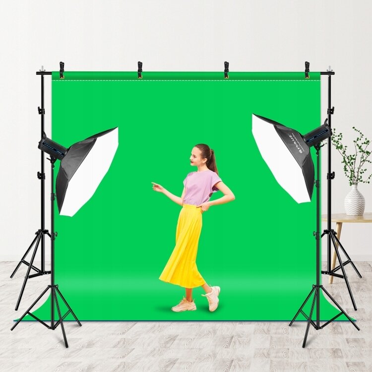 Na zdjęciu znajduje się zestaw do studia fotograficznego z zielonym tłem, dwoma lampami studyjnymi i statywami. Na tle stoi osoba ubrana w różową koszulkę i żółtą spódnicę.