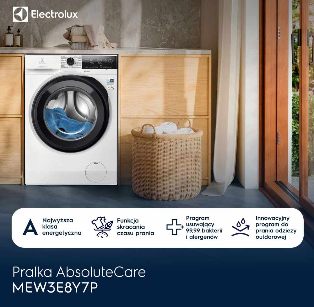 Na obrazie znajduje się pralka Electrolux w zabudowie kuchennej, z widocznym logo Electrolux. Obok pralki stoi kosz z praniem, a na dole widnieje napis: \'Pralka AbsoluteCare MEW3E8Y7P\'.