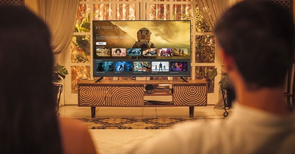 Telewizor wyświetla ekran główny z filmem \'Beyond Space\' oraz miniaturami innych filmów. W tle widać zasłony i roślinność za oknem.