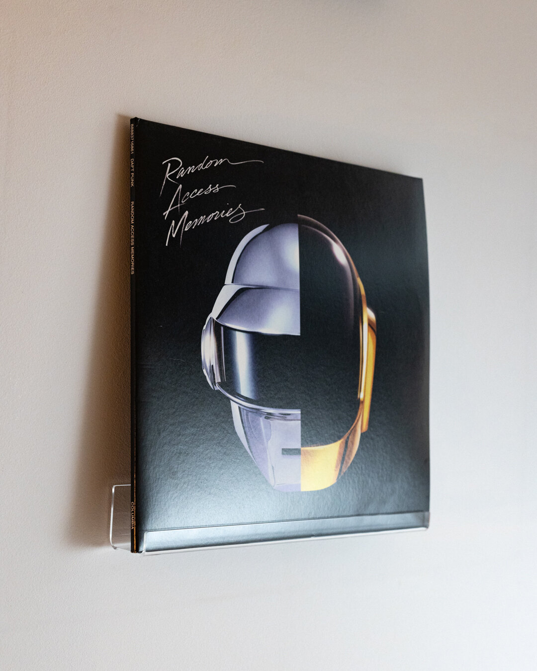 Na ścianie zamontowana jest przezroczysta półka, na której znajduje się okładka płyty winylowej z napisem \'Random Access Memories\' i grafiką przedstawiającą hełm.