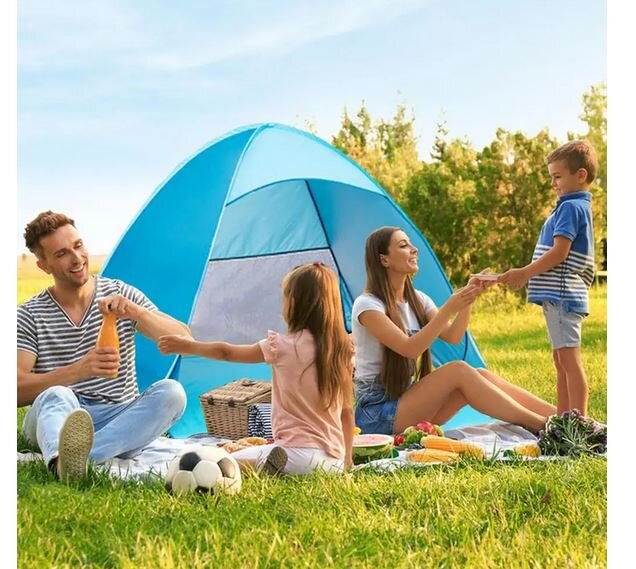 Na trawie rozłożony jest niebieski namiot plażowy, a przed nim siedzą cztery osoby na kocu z piknikowym jedzeniem i piłką. W tle widać drzewa i jasne niebo.