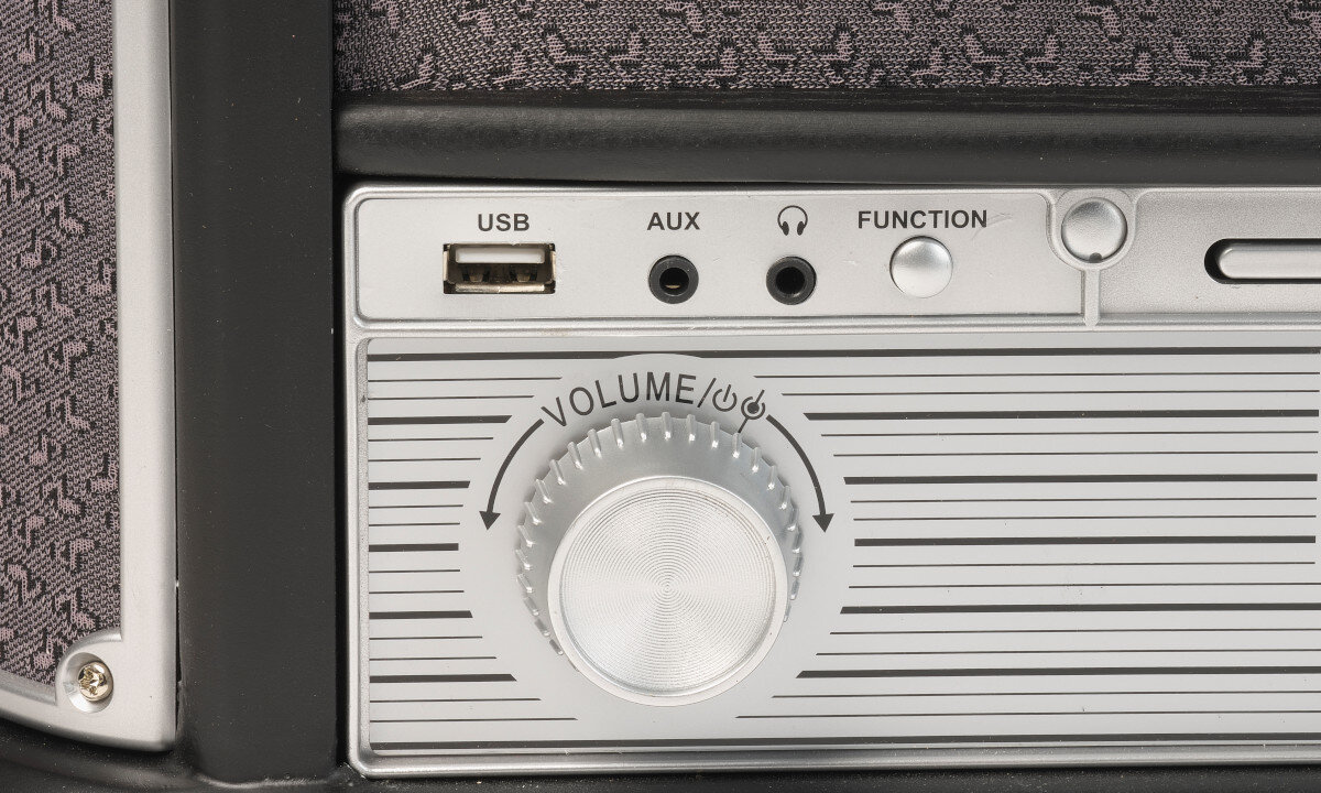 Panel urządzenia z portem USB, wejściem AUX, gniazdem słuchawkowym, przyciskiem FUNCTION oraz pokrętłem VOLUME z oznaczeniami kierunku zwiększania i zmniejszania głośności.