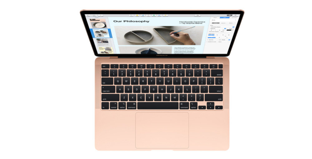 Laptop z otwartym ekranem, na którym widoczny jest dokument z tekstem \'Our Philosophy\' oraz zdjęciami. Klawiatura jest czarna z jasnymi klawiszami funkcyjnymi.