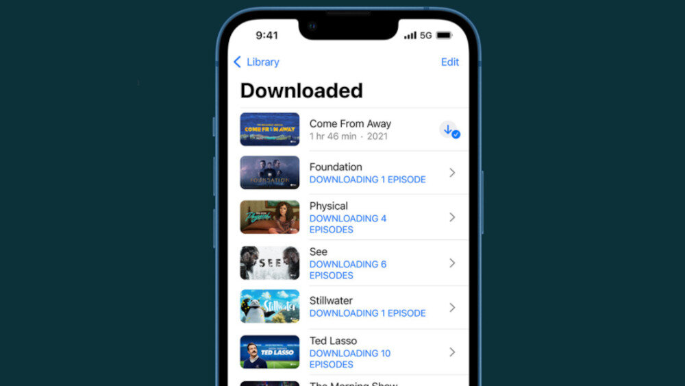 Ekran smartfona wyświetla listę pobranych treści z aplikacji, z tytułami takimi jak \'Come From Away\', \'Foundation\', \'Physical\', \'See\', \'Stillwater\', \'Ted Lasso\' i \'The Morning Show\'. Widoczny jest także status pobierania odcinków dla niektórych tytułów.