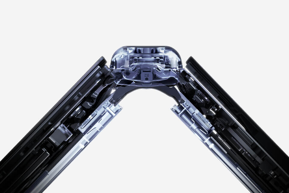 Obraz przedstawia zbliżenie na zawias składanej konstrukcji urządzenia elektronicznego, prawdopodobnie smartfona. Widoczne są metalowe i plastikowe elementy mechanizmu na jasnym tle.