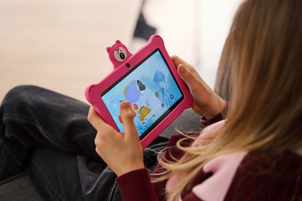 Dziecko trzyma różowy tablet z kolorowym ekranem, na którym wyświetlane są postacie zwierząt. Tablet ma obudowę z uszami i ozdobą przypominającą misia.