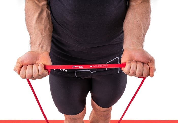 Osoba trzyma czerwoną gumę oporową z widocznym logo \'HOP SPORT\' i oznaczeniem oporu \'7-16kg\'.