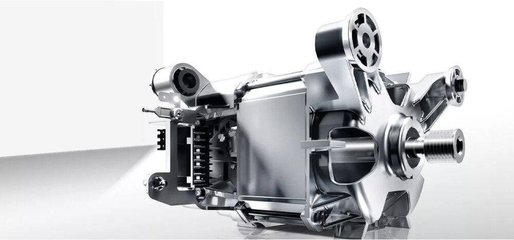 Obraz przedstawia metalowy element mechaniczny, prawdopodobnie część silnika, z widocznymi zębatkami i śrubami. Element ma błyszczące, srebrne wykończenie.