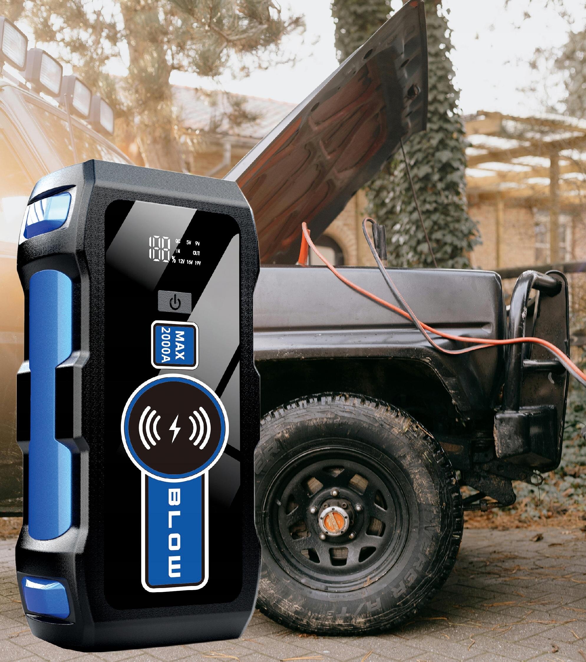 Na pierwszym planie widoczny jest czarno-niebieski powerbank z napisem \'MAX 2000A BLOW\', a w tle samochód z otwartą maską i podłączonymi kablami rozruchowymi.