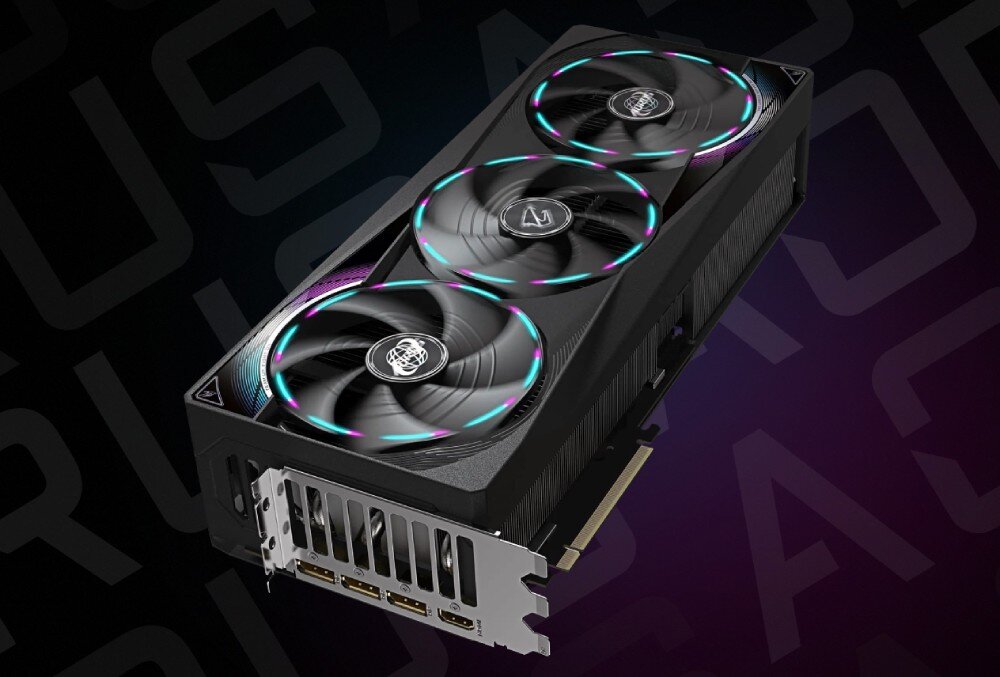 Na obrazie widoczna jest karta graficzna z trzema wentylatorami, z podświetleniem RGB na czarnym tle. Na karcie znajduje się logo producenta, a w tle widoczny jest napis \'AORUS\'.