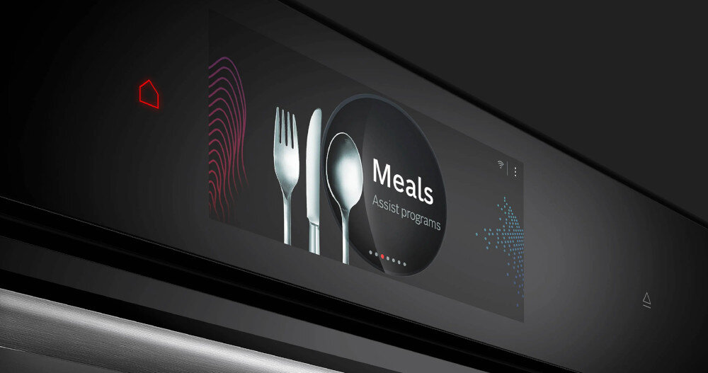 Zbliżenie na panel sterowania piekarnika z wyświetlaczem dotykowym, na którym widoczny jest napis \'Meals Assist programs\' oraz ikony sztućców. Obok znajduje się czerwony symbol domu.