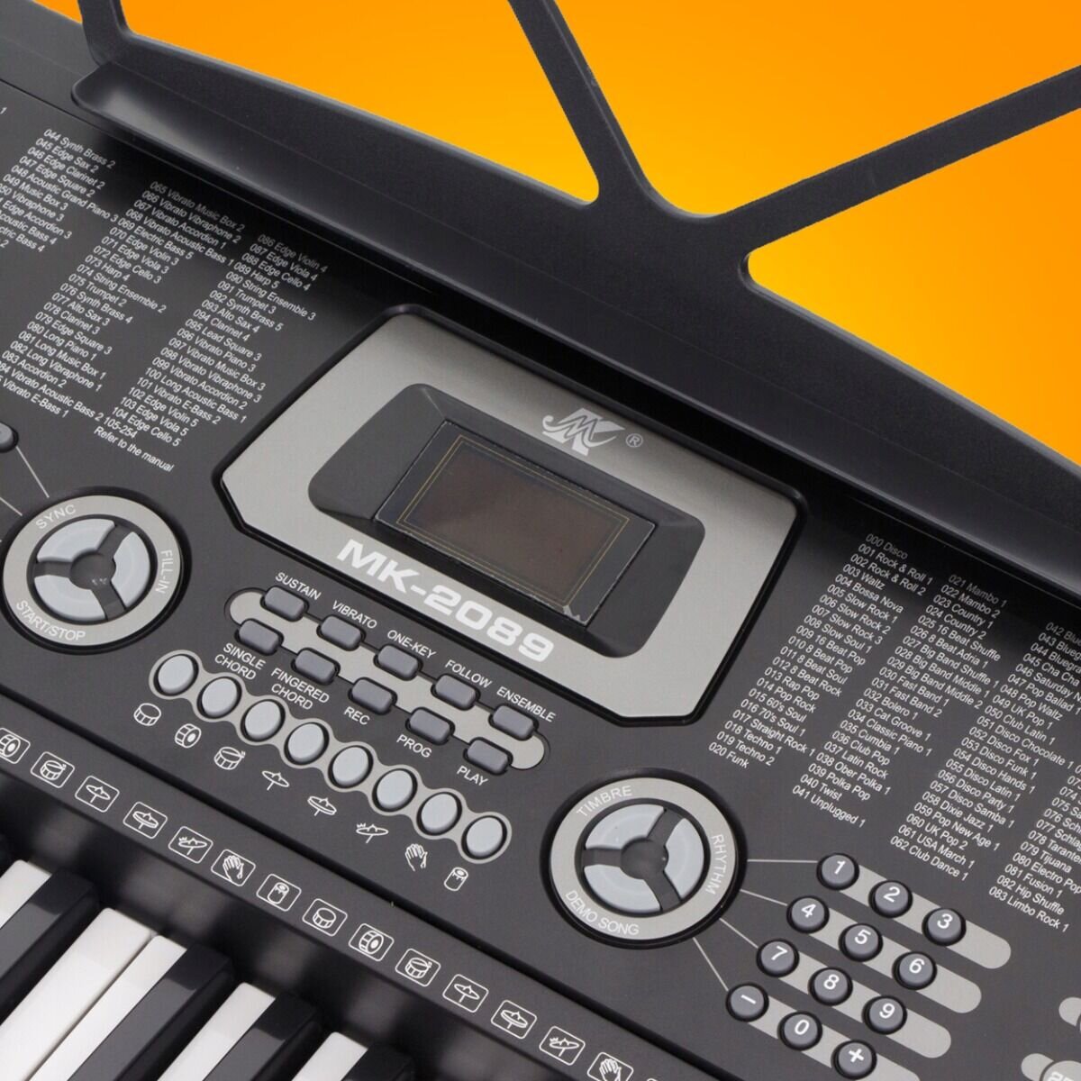 Zbliżenie na panel sterowania keyboardu z wyświetlaczem oznaczonym jako \'MK-2089\'. Wokół wyświetlacza znajdują się różne przyciski funkcyjne oraz pokrętła, a w tle widoczny jest pomarańczowy kolor.