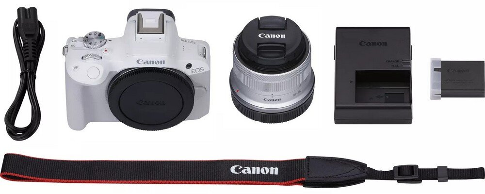 Na obrazie znajduje się biały aparat bezlusterkowy z logo \'Canon\', obiektyw, ładowarka, bateria, pasek z napisem \'Canon\' oraz kabel zasilający.