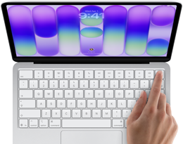 Laptop z otwartym ekranem wyświetlającym kolorowe gradienty i godzinę 9:41. Na klawiaturze widoczna jest dłoń dotykająca klawisza.
