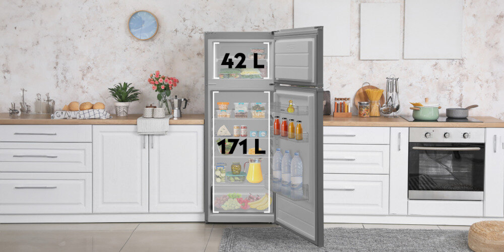 Kuchnia z otwartą lodówką w kolorze inox, na której drzwiach widoczne są napisy \'42 L\' i \'171 L\'. Wnętrze lodówki zawiera różne produkty spożywcze, a na blacie kuchennym znajdują się naczynia i dekoracje.