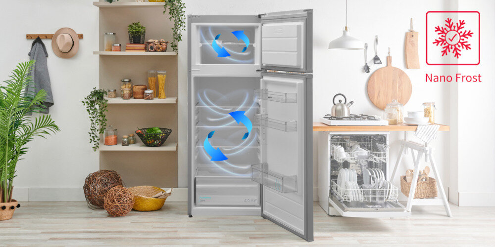 Otwarta lodówka z widocznym systemem Nano Frost, oznaczonym niebieskimi strzałkami wewnątrz. Obok lodówki znajduje się kuchnia z otwartą zmywarką i półką z roślinami oraz naczyniami.