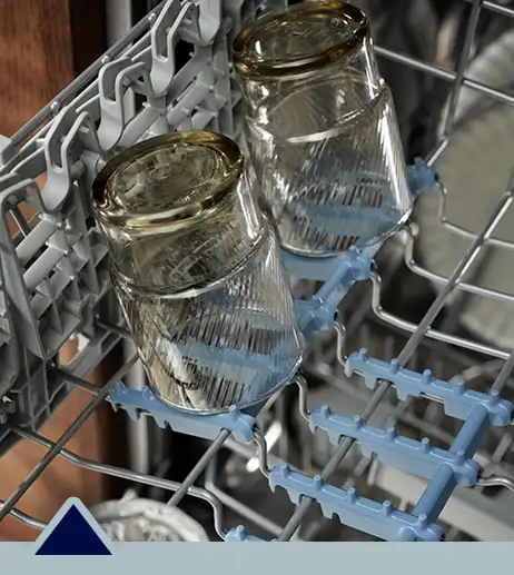 Wnętrze zmywarki z widocznymi dwoma szklankami umieszczonymi do góry dnem na górnym koszu. Kosz ma szare i niebieskie elementy plastikowe do stabilizacji naczyń.