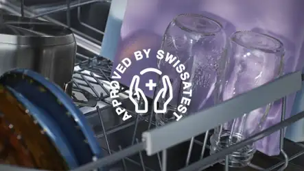 Wnętrze zmywarki z widocznymi szklankami i naczyniami. Na obrazie znajduje się tekst: \'APPROVED BY SWISSTEST\'.