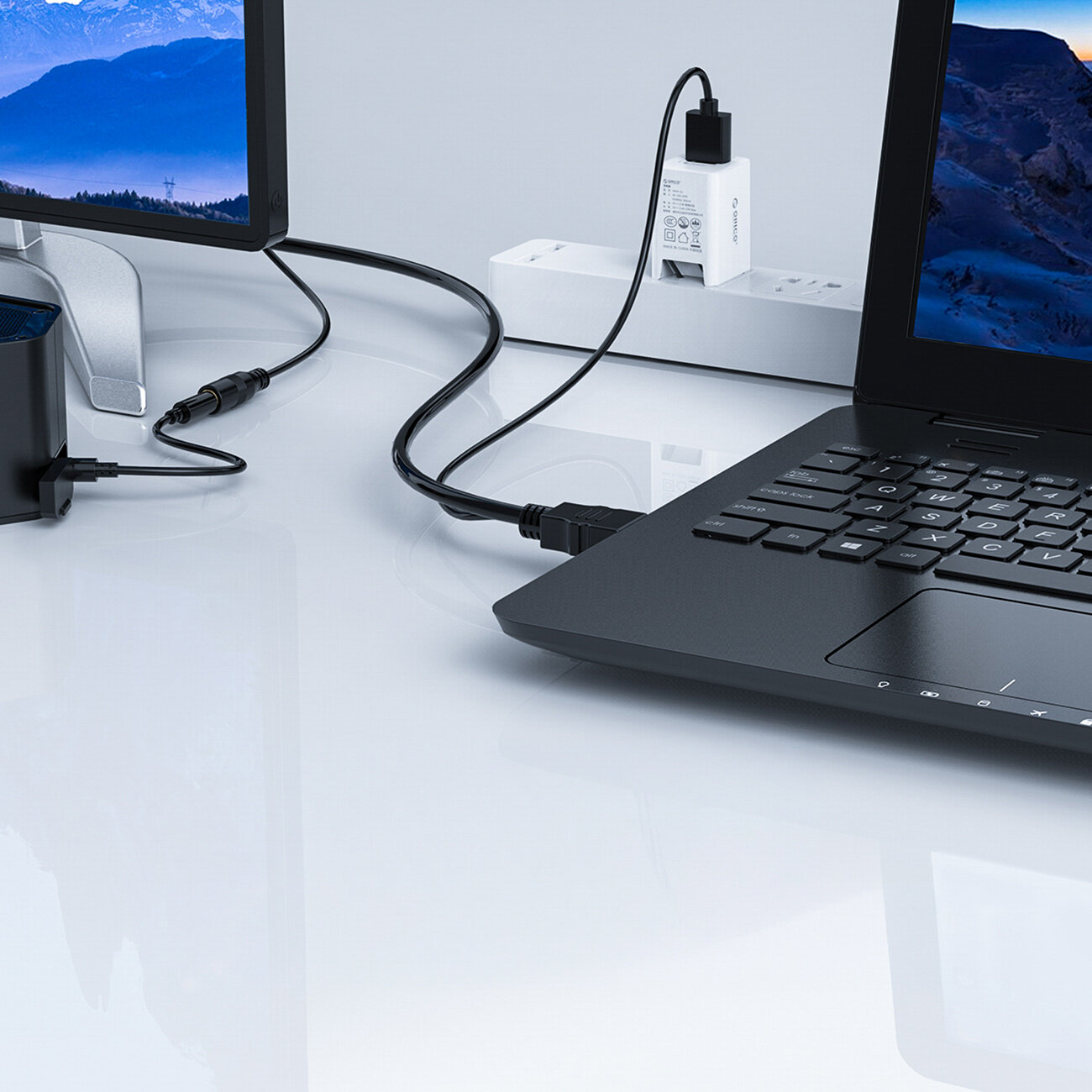 Na biurku znajduje się laptop podłączony kablem do monitora oraz zasilacz USB wpięty do listwy zasilającej. Kabel jest czarny i ma kilka złączy, w tym HDMI i USB.