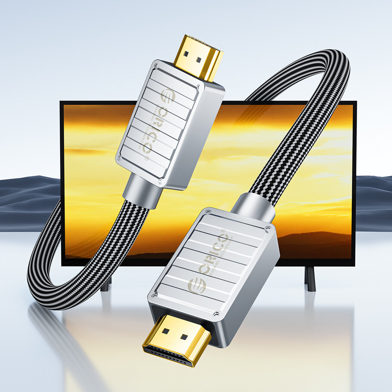 Na obrazie widoczny jest czarny kabel HDMI z metalowymi końcówkami, na których znajduje się logo \'Orico\'. W tle znajduje się ekran z krajobrazem o zachodzie słońca.