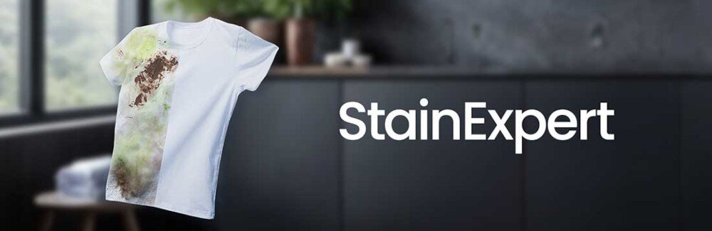 Na obrazie widoczna jest biała koszulka z dużymi plamami, obok której znajduje się napis \'StainExpert\'. W tle widać rozmyty obraz wnętrza z ciemnymi meblami.