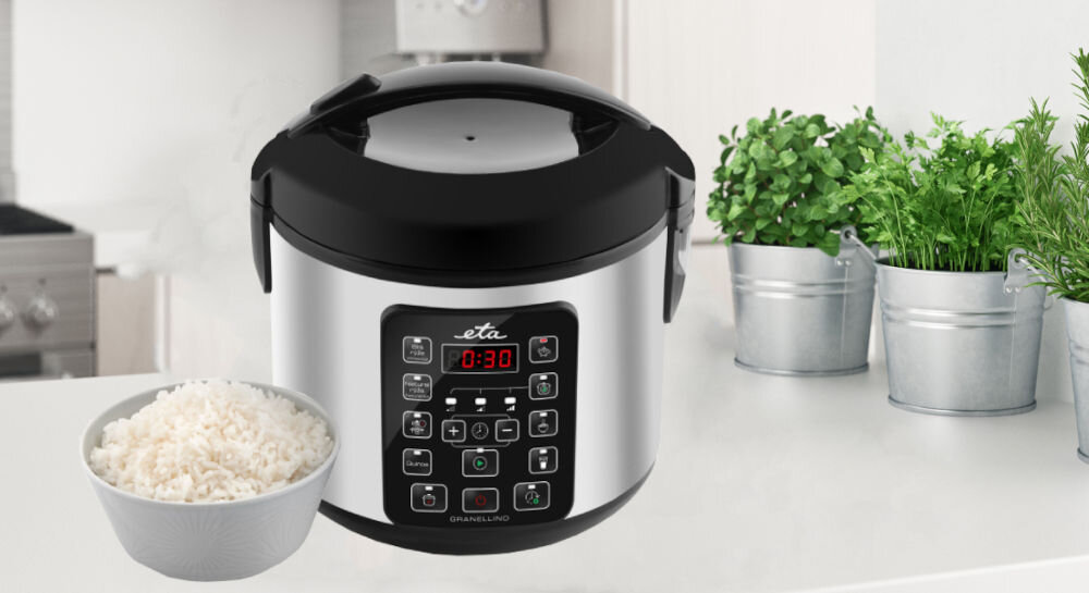 Na blacie kuchennym stoi multicooker z wyświetlaczem pokazującym \'0:30\' oraz miska z ugotowanym ryżem. W tle widoczne są doniczki z zielonymi roślinami.