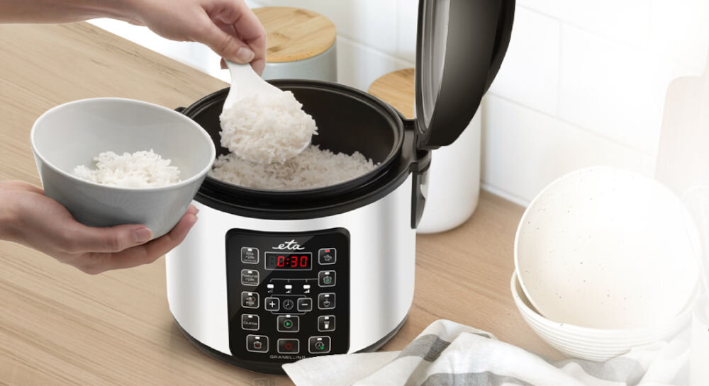Na blacie kuchennym stoi multicooker z otwartą pokrywą, wypełniony ryżem. Na panelu sterowania widoczny jest wyświetlacz z czasem 8:30 oraz przyciski funkcyjne.