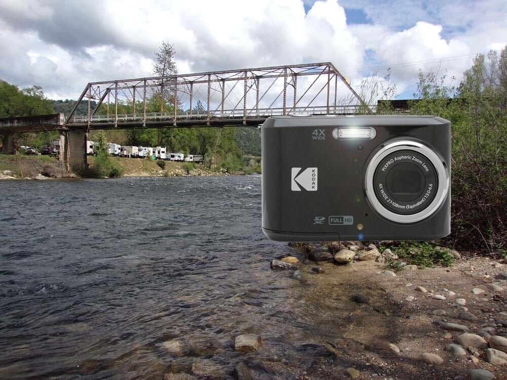 Na obrazie widać aparat fotograficzny z logo KODAK, umieszczony na tle rzeki i mostu. Aparat ma oznaczenia 4X WIDE i FULL HD.
