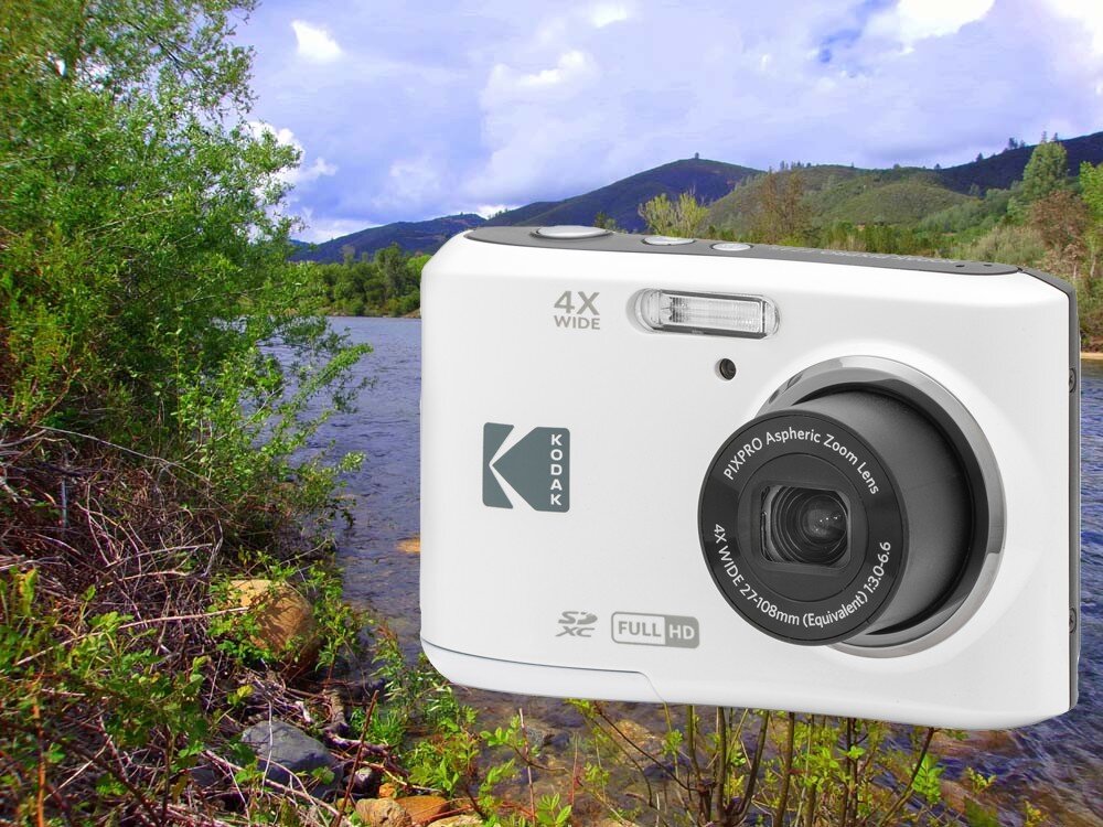 Na tle krajobrazu z rzeką i wzgórzami widoczny jest biały aparat fotograficzny z logo Kodak. Na aparacie znajdują się napisy: \'4X WIDE\', \'SD XC\', \'FULL HD\' oraz \'PIXPRO Aspheric Zoom Lens 4X WIDE 27-108mm (Equivalent) 1:3.6-6\'.