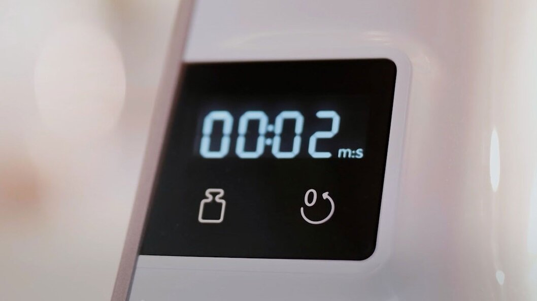 Wyświetlacz elektroniczny pokazuje czas 00:02 m:s. Pod ekranem znajdują się ikony wagi i przycisku z symbolem uśmiechu.