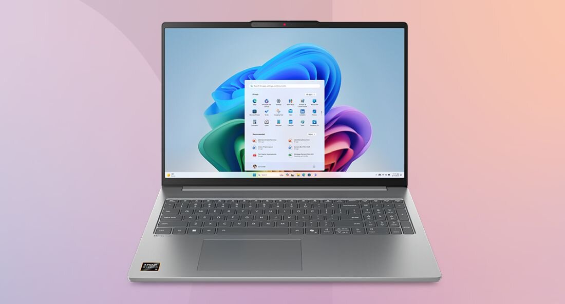 Na obrazie widoczny jest laptop z otwartym ekranem, na którym wyświetlany jest pulpit systemu Windows 11 z ikonami aplikacji. Na obudowie laptopa znajduje się logo producenta oraz naklejka z oznaczeniem procesora.