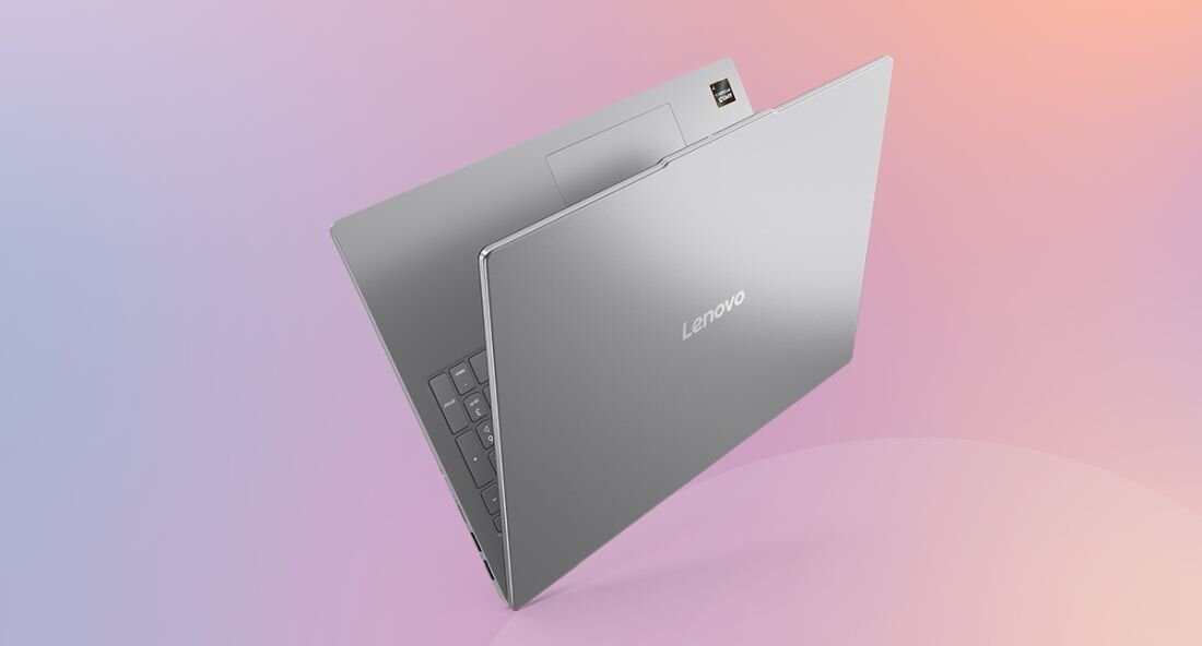 Na obrazie widać otwarty laptop w kolorze srebrnym z widocznym logo \'Lenovo\' na pokrywie. Tło jest gradientowe, przechodzące od różowego do fioletowego.