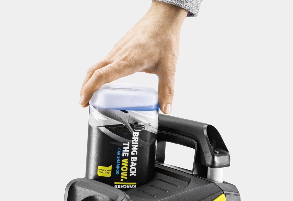 Ręka trzyma pojemnik z napisem \'BRING BACK THE WOW CAR SHAMPOO\' umieszczony na uchwycie urządzenia KARCHER. Widoczne jest logo KARCHER na pojemniku.