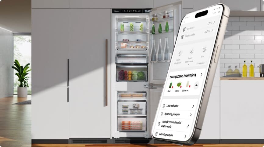 Otwarta lodówka z widocznymi półkami wypełnionymi produktami spożywczymi, obok której znajduje się duży smartfon z aplikacją do zarządzania żywnością. W tle widać nowoczesne wnętrze kuchni z rośliną i butelkami na blacie.
