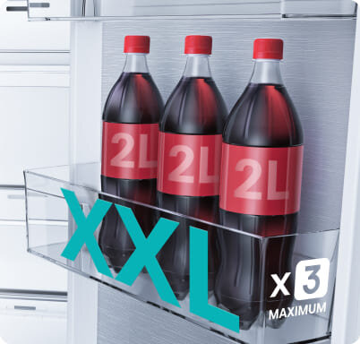 Trzy butelki napoju o pojemności 2L każda, umieszczone w przezroczystej półce lodówki. Na obrazie widoczny jest napis \'XXL x3 MAXIMUM\'.