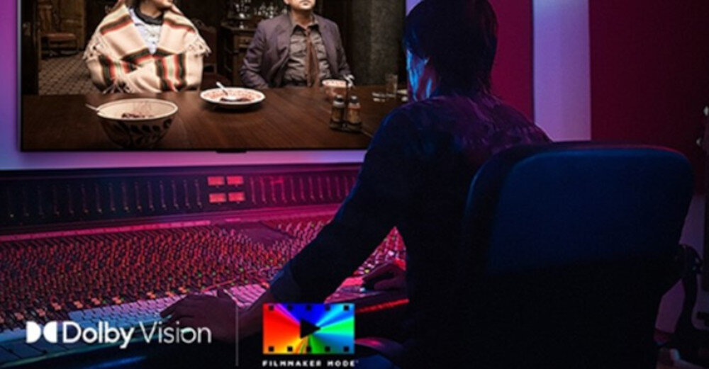 Osoba siedzi przed dużym ekranem, na którym wyświetlany jest film. Na dole ekranu widoczne są loga \'Dolby Vision\' i \'Filmmaker Mode\'.