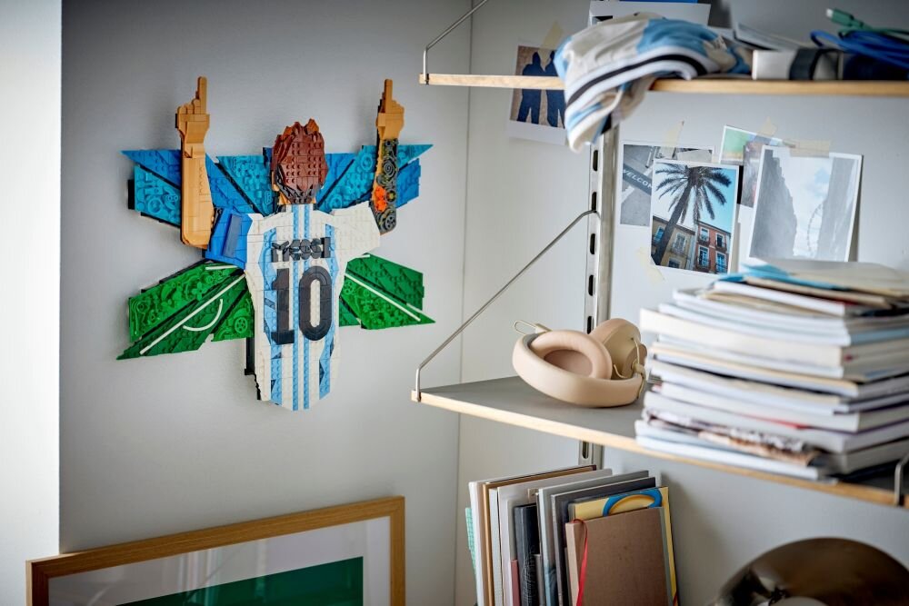 Na ścianie wisi mozaika z klocków LEGO przedstawiająca piłkarza w koszulce z numerem 10 i napisem \'Messi\'. Obok znajdują się półki z książkami, słuchawkami i zdjęciami.
