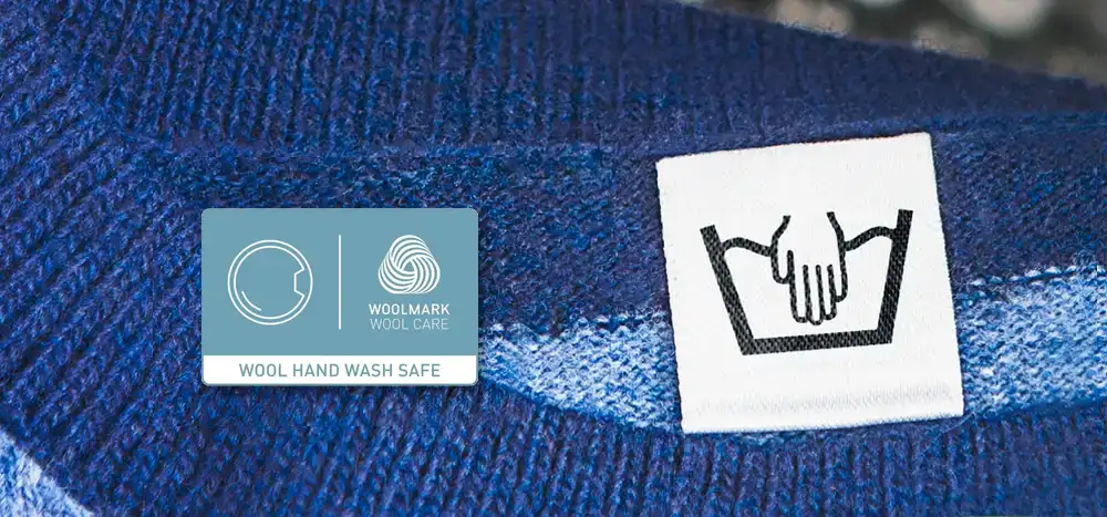 Na obrazie widoczna jest metka z symbolem prania ręcznego oraz etykieta z napisem \'WOOL HAND WASH SAFE\' i logo \'WOOLMARK WOOL CARE\'.