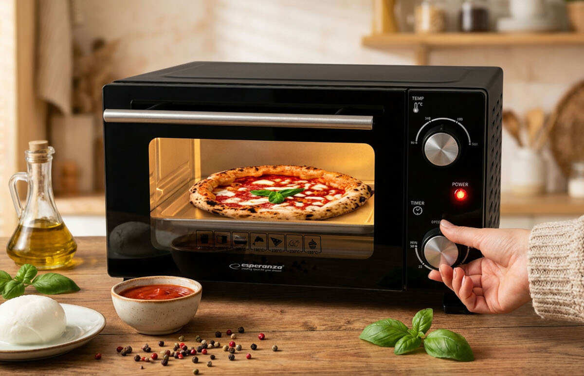 Czarny mini piekarnik z logo \'esperanza\' na froncie, w którym piecze się pizza. Obok piekarnika znajdują się składniki do pizzy, a ręka reguluje pokrętło na panelu sterowania.