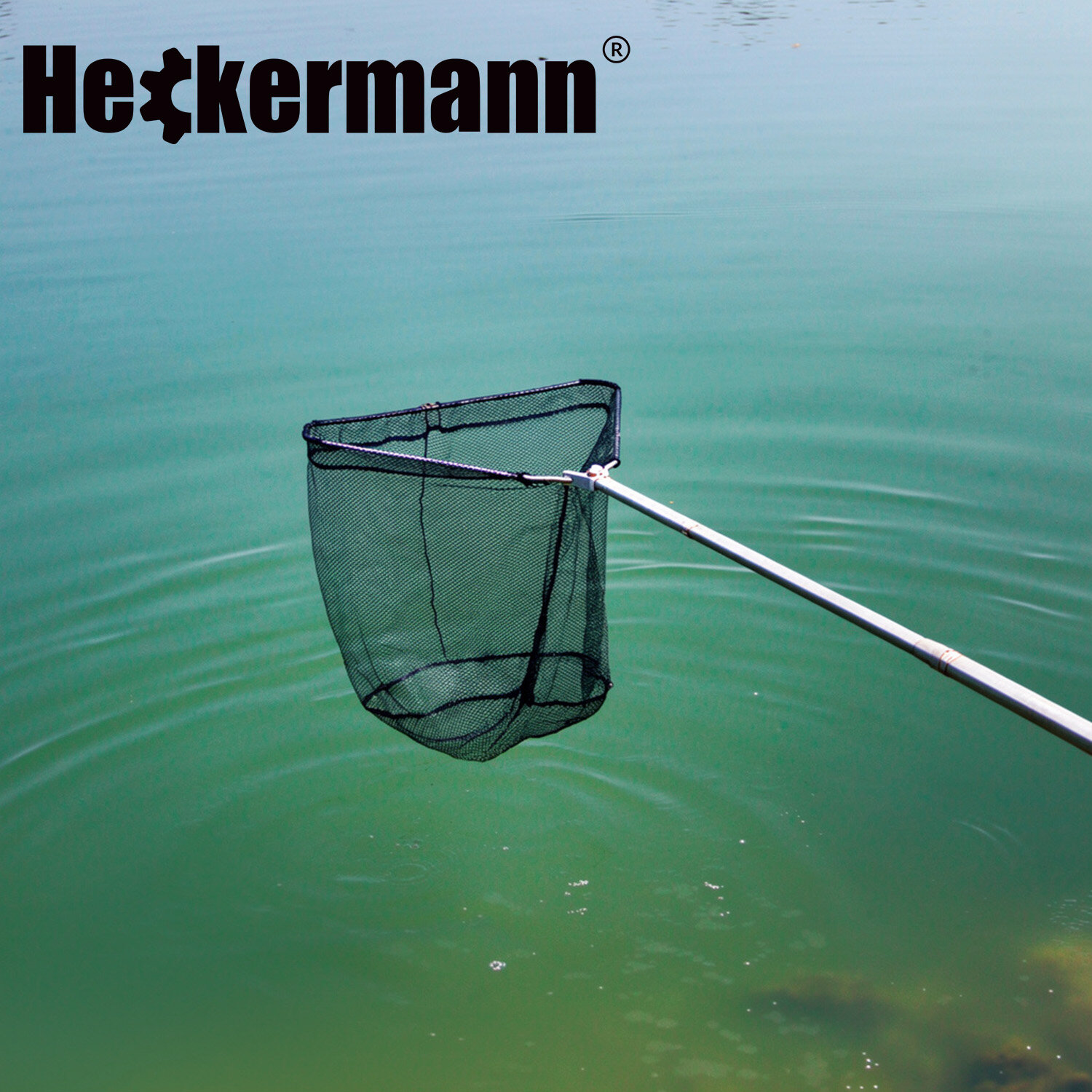 Podbierak teleskopowy z czarną siatką jest zanurzony w zielonkawej wodzie. W górnej części obrazu widoczne jest logo \'Heckermann\'.