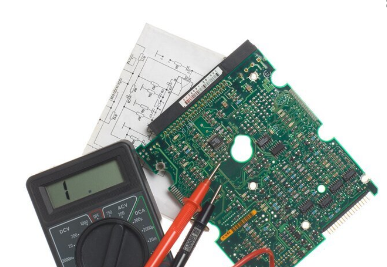 Na obrazie widoczny jest cyfrowy multimetr z wyświetlaczem pokazującym cyfrę \'1\', obok którego znajduje się zielona płytka drukowana oraz schemat elektroniczny. Multimetr ma czerwone i czarne przewody pomiarowe.