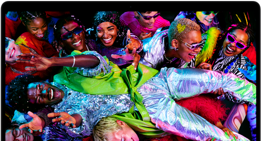 Grupa osób ubranych w kolorowe, błyszczące stroje bawi się razem, uśmiechając się i gestykulując. Tło jest żywe i pełne energii, z różnorodnymi kolorami i wzorami.