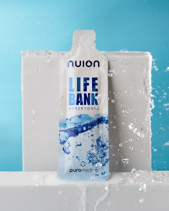Na obrazie widoczna jest saszetka z napisem \'LIFE BANK HYPERTONIC\' oraz \'puromedica\'. W tle widać niebieskie tło i krople wody.