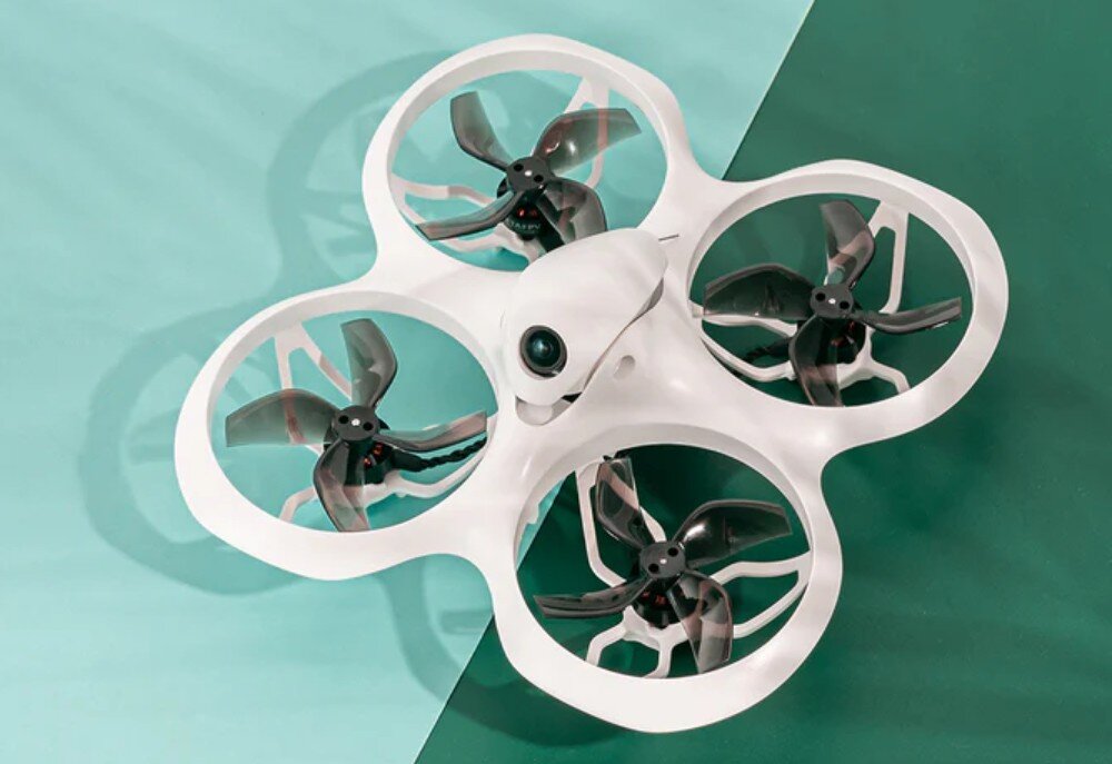 Na obrazie widoczny jest biały dron z czterema śmigłami, umieszczony na tle w dwóch odcieniach zieleni. Dron ma kamerę z przodu i osłony wokół śmigieł.