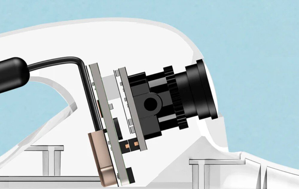 Ilustracja przedstawia zbliżenie na komponenty elektroniczne i kamerę zamontowane wewnątrz obudowy urządzenia. Widoczny jest przewód podłączony do płytki drukowanej oraz obiektyw kamery.