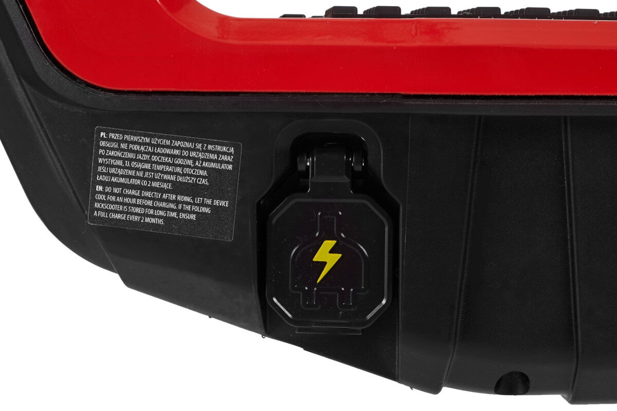 Czarno-czerwony element hulajnogi elektrycznej z widocznym gniazdem ładowania oznaczonym żółtą błyskawicą. Obok znajduje się tabliczka z instrukcją w języku polskim i angielskim dotyczącą ładowania urządzenia.