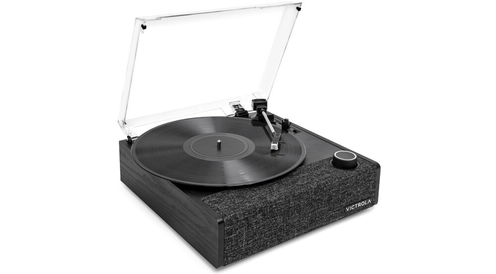 Na obrazie widoczny jest czarny gramofon z przezroczystą pokrywą i czarną płytą na talerzu. Na froncie urządzenia znajduje się logo \'VICTROLA\'.