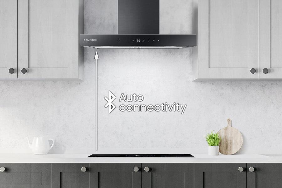 Łączność Bluetooth - duże ułatwienie - Samsung NK24C5703TM Kuchnia z zamontowanym okapem marki Samsung nad płytą grzewczą. Na ścianie widoczny jest tekst \'Auto connectivity\' z symbolem Bluetooth.
