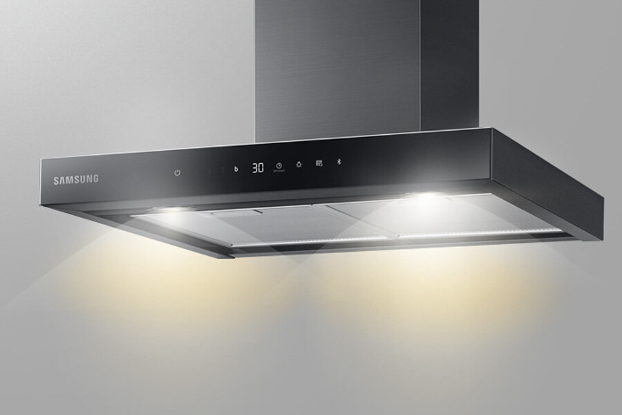 Oświetlenie LED w Samsung NK24C5703TM - oszczędność energii Na obrazie widoczny jest okap kuchenny w kolorze grafitowej stali z podświetleniem. Na panelu sterowania znajduje się logo \'SAMSUNG\' oraz cyfry i ikony wskazujące ustawienia.