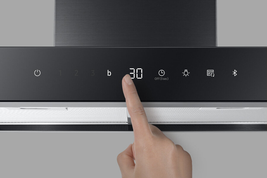 Intuicyjny panel dotykowy ułatwia sterowanie Samsung NK24C5703TM Panel sterowania okapu z wyświetlaczem pokazującym liczbę \'30\' oraz ikonami funkcji, takich jak włącznik, timer, oświetlenie i Bluetooth. Palec dotyka panelu w okolicy wyświetlacza.